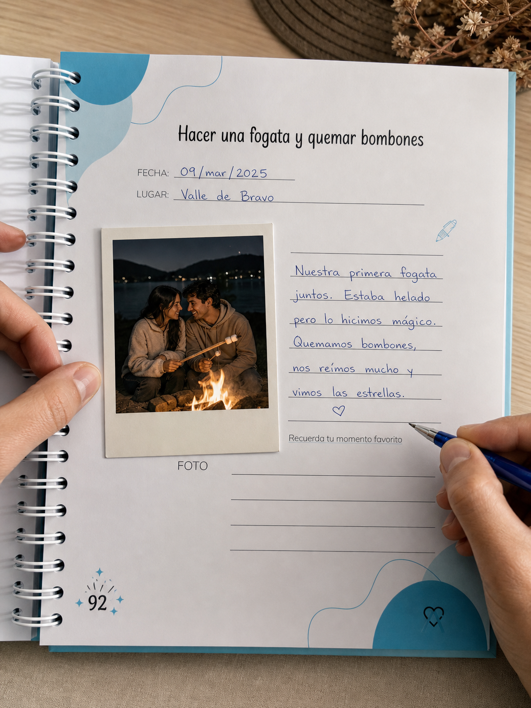 Mano escribiendo en la página de la experiencia fogata con polaroid pegada